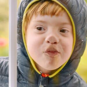 Child with dx of Down syndrome with nose pressed against a window.