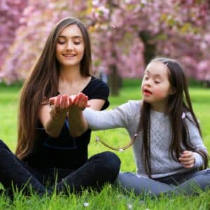 Girl and mother at the park sitting in grass in spring exploring a butterfly. Girl has a diagnosis of Down syndrome.