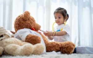 Little girl pretending to be a doctor with a large brown Teddy bear.